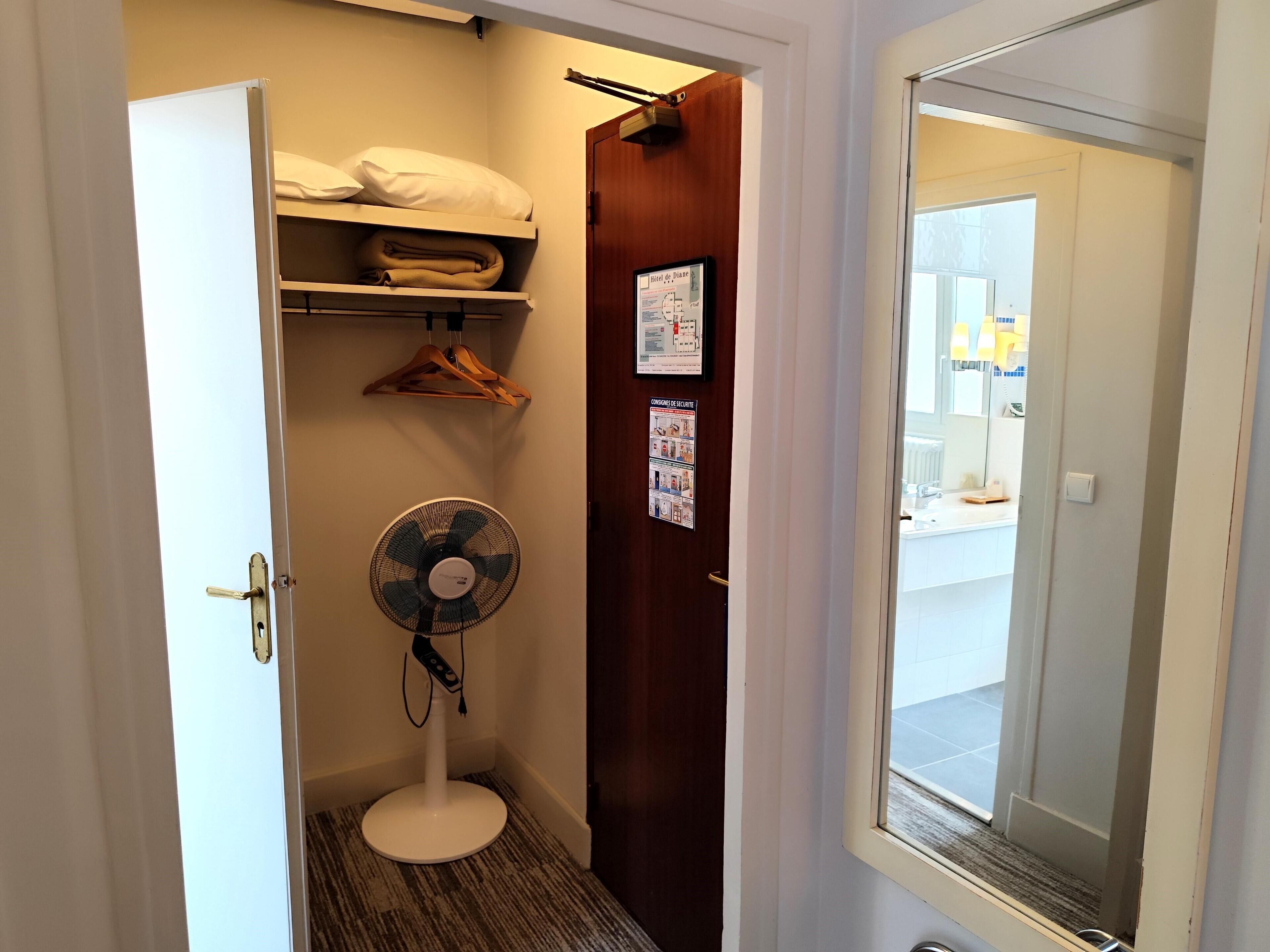 Quarto de hotel com cama, ventilador, cabideiro e porta para um banheiro.