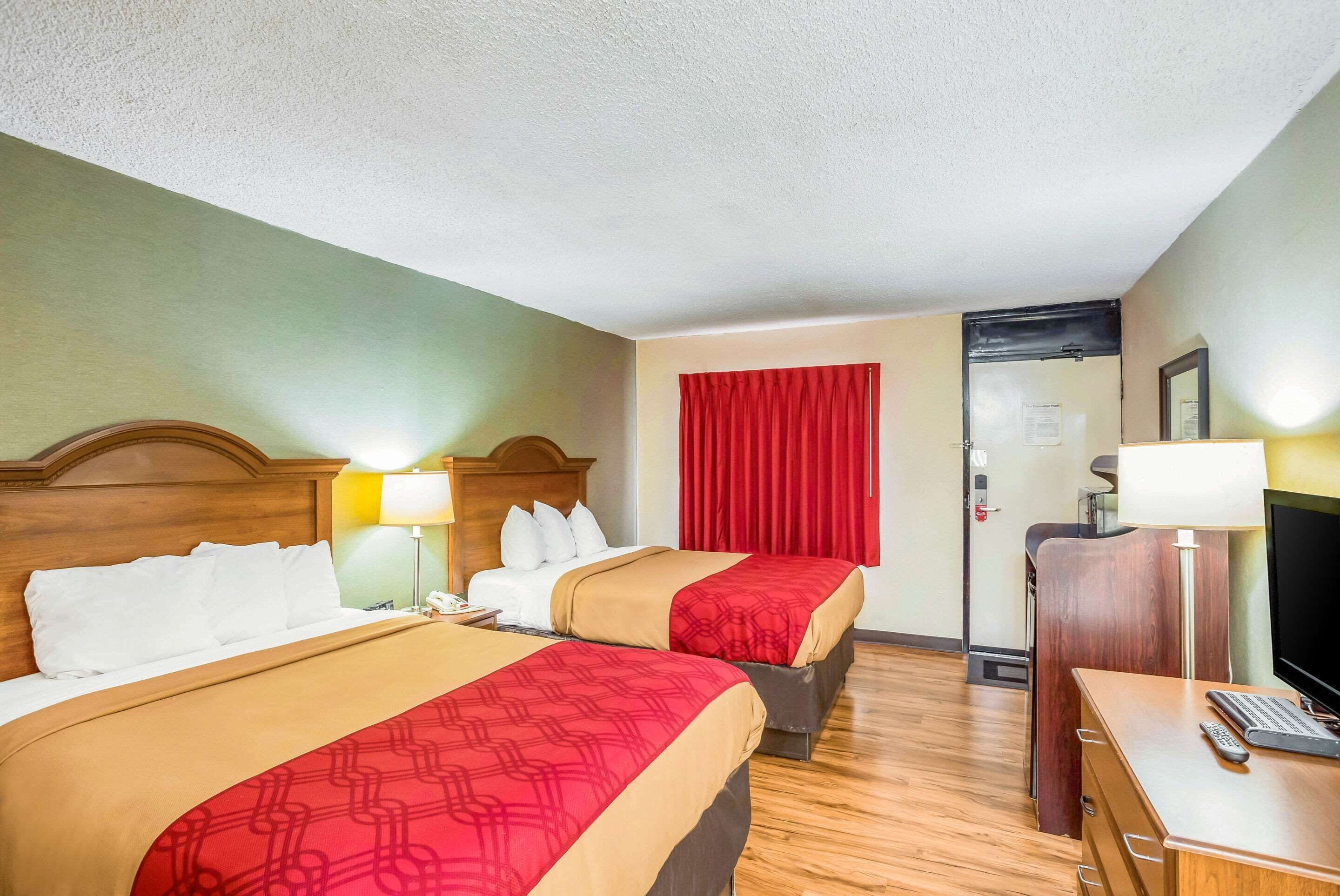 A hotel room with two beds, a desk with a computer, a TV, and a red curtain.