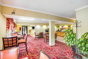 A hotel lobby with a red patterned carpet, multiple seating areas, a reception desk, and a large green plant. - Econo Lodge Huntington - Barboursville University Area (Huntington)