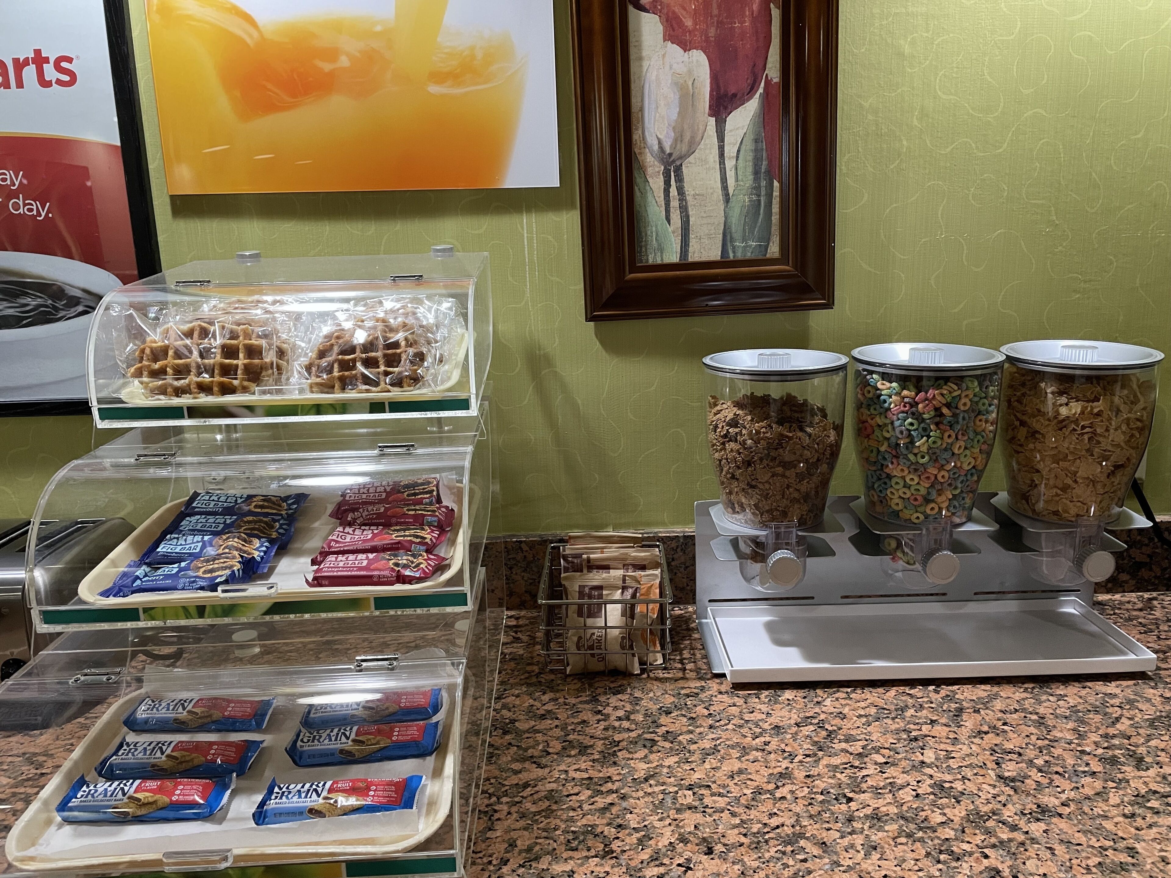 A breakfast buffet with waffles, cereal, and granola bars.