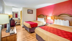 A hotel room with two beds, a desk with a computer, a mirror, and a red wall.