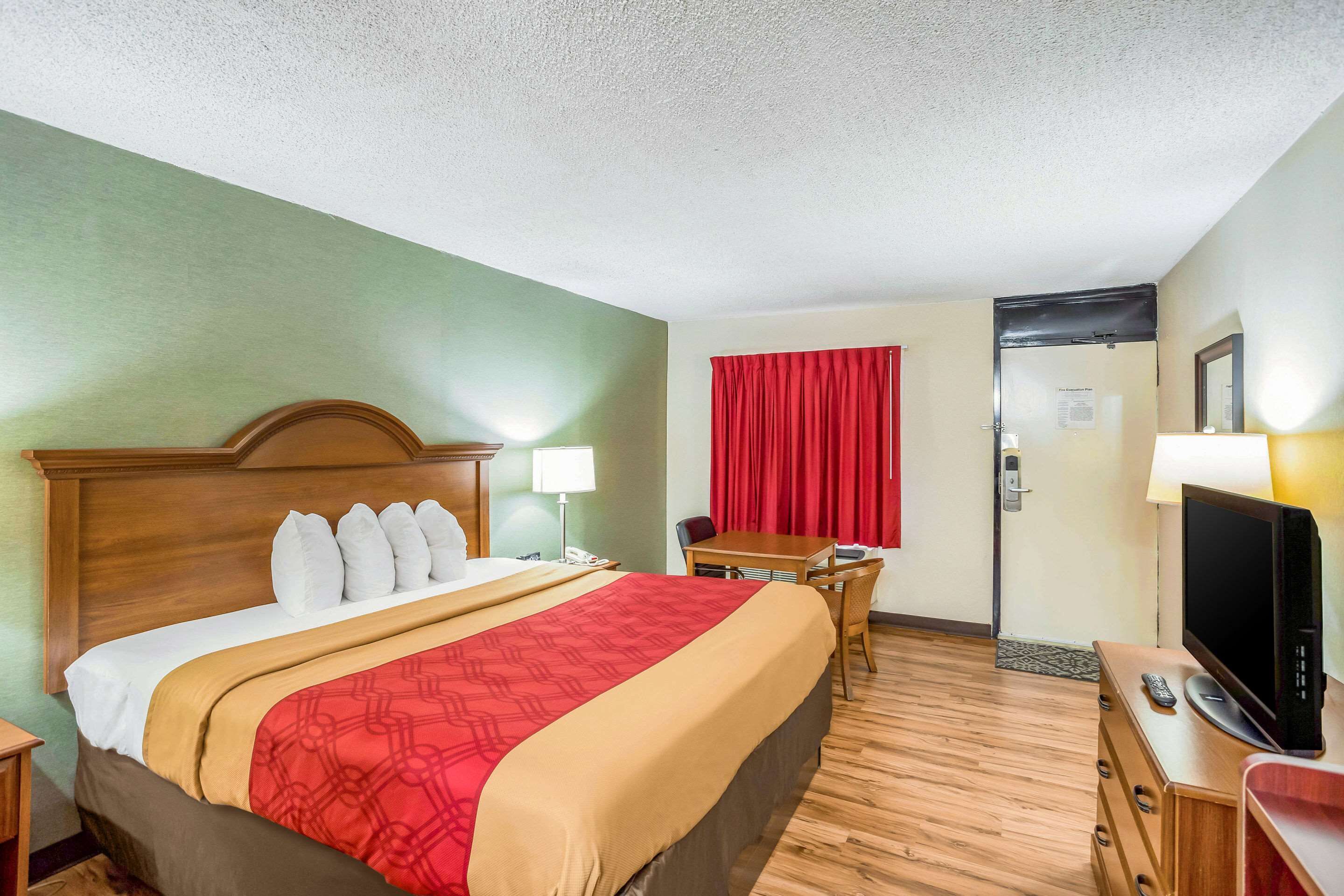 A hotel room with a bed, a desk, a television, and a door.