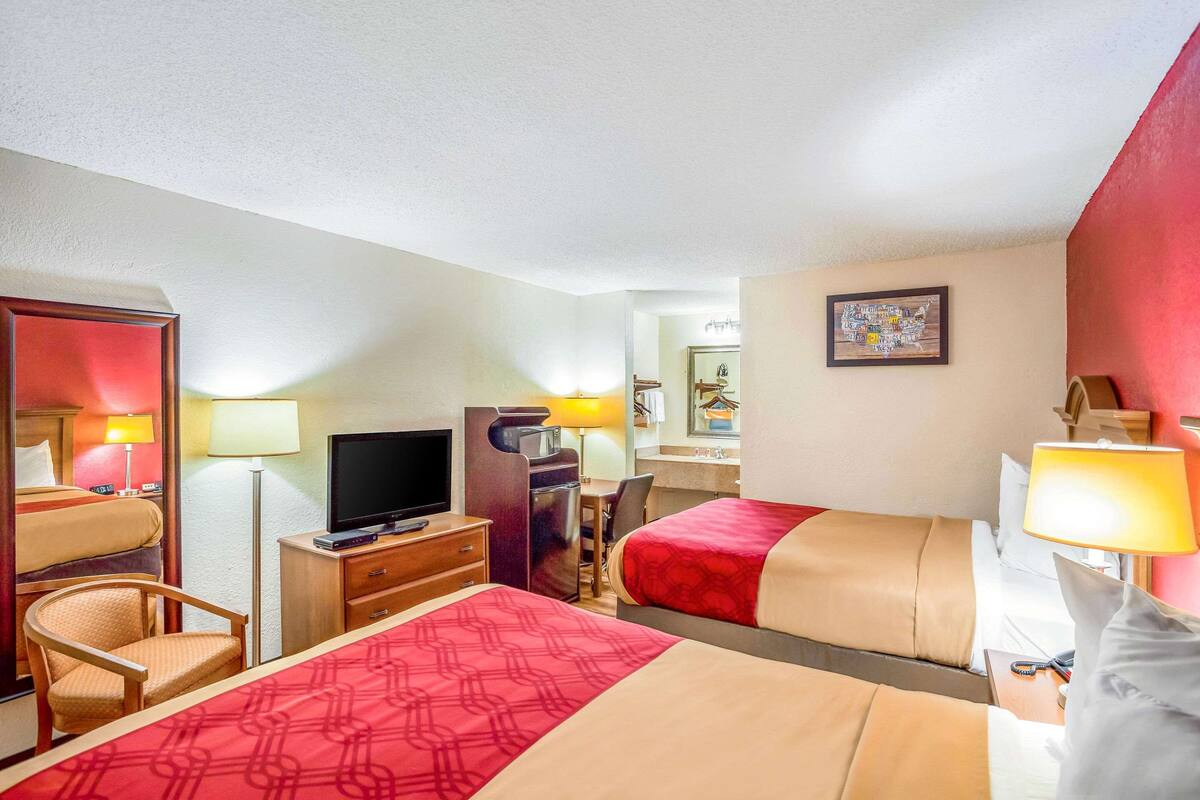 A hotel room with two beds, a desk, a television, and a chair.