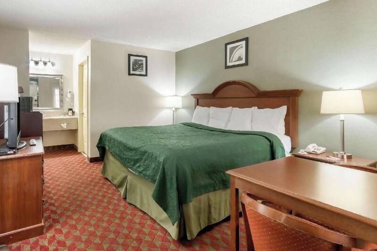 A hotel room with a bed, a desk, a chair, a television, and a bathroom.