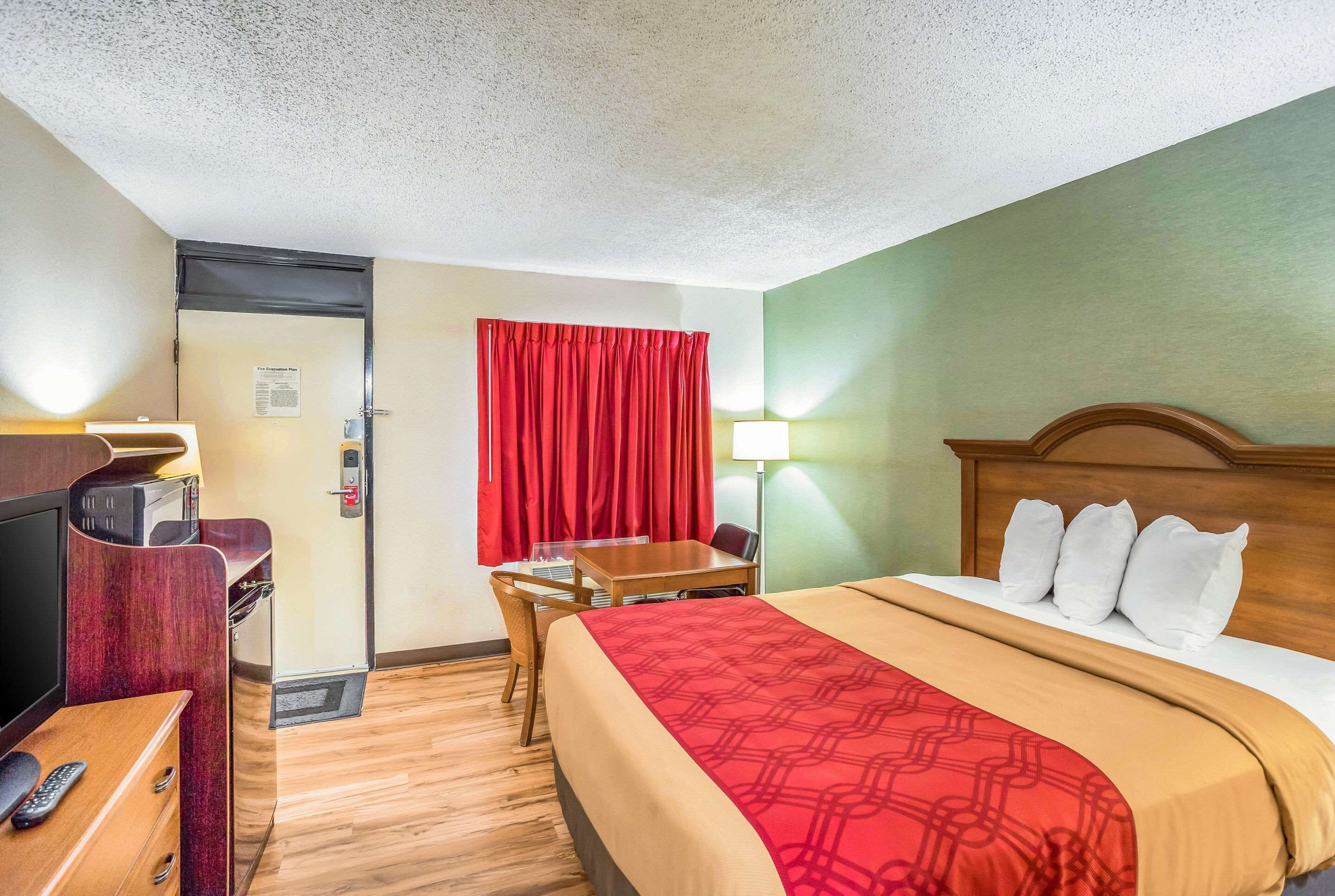 Ein Hotelzimmer mit Bett, Schreibtisch mit Stuhl, Fernseher und einer Tür.