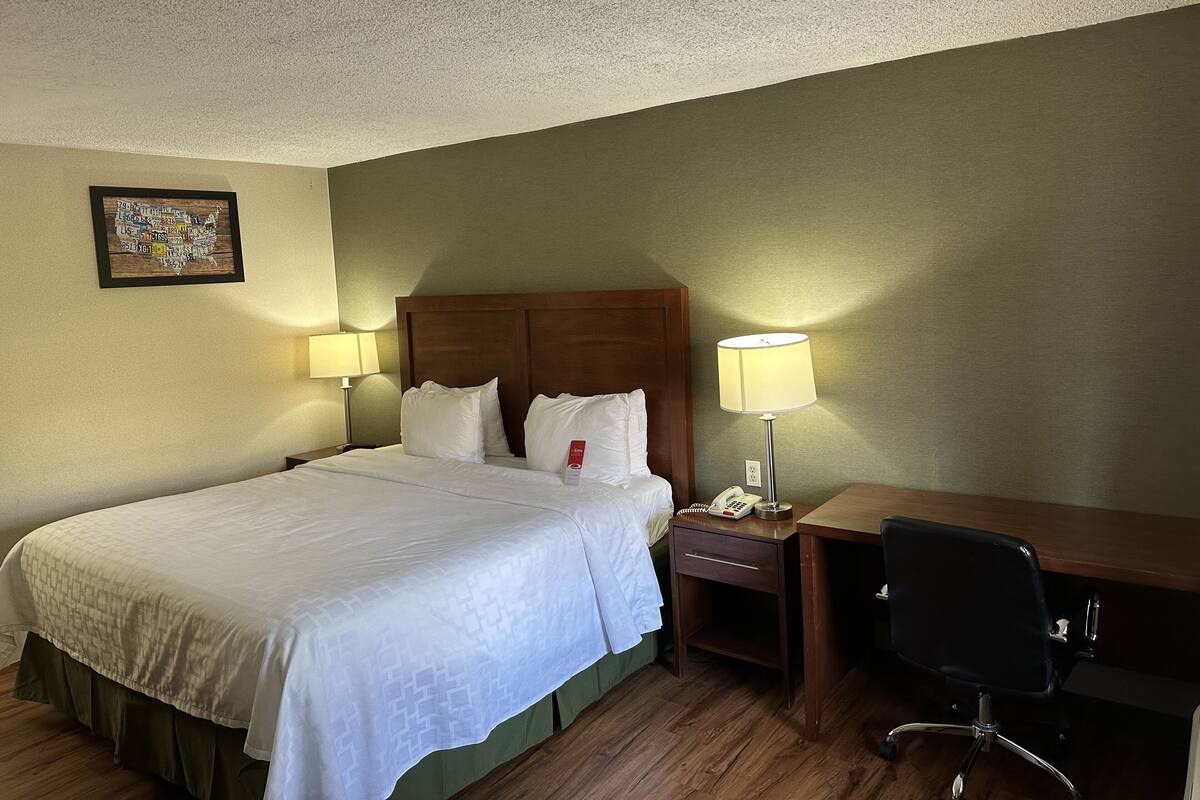 A hotel room with a large bed, two bedside tables with lamps, a desk with a chair, and a wall-mounted telephone.