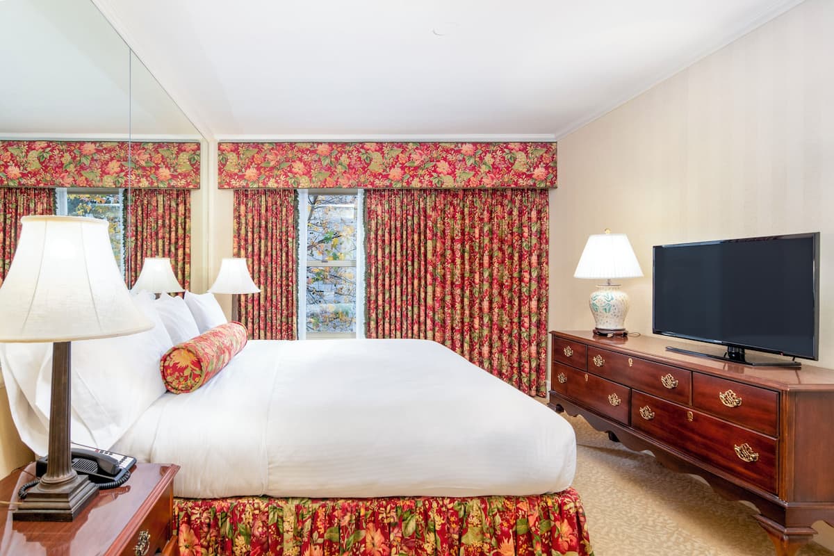 A hotel room with a large bed, two bedside lamps, a television on a wooden cabinet, and floral curtains.