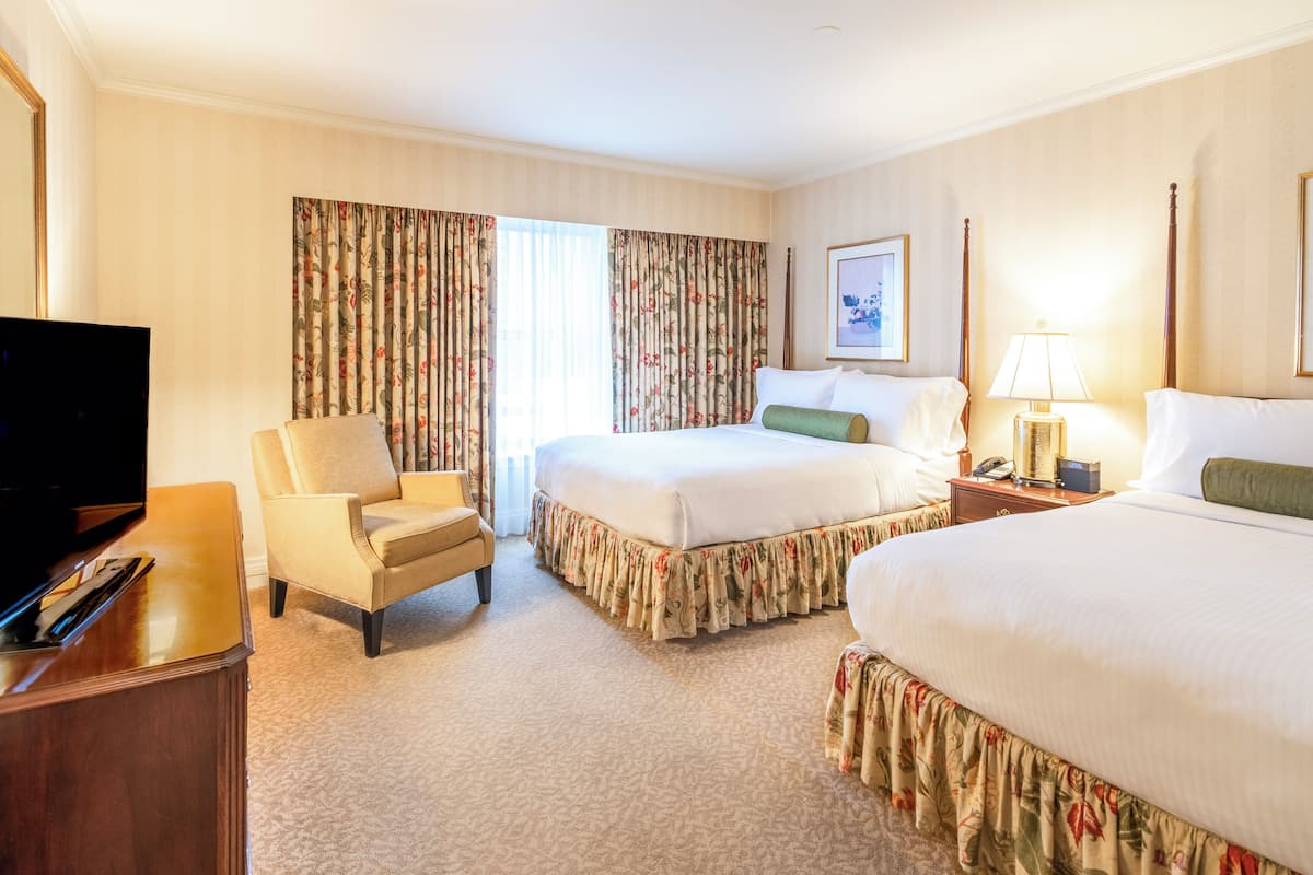 A hotel room with two beds, a TV, a chair, and a desk.