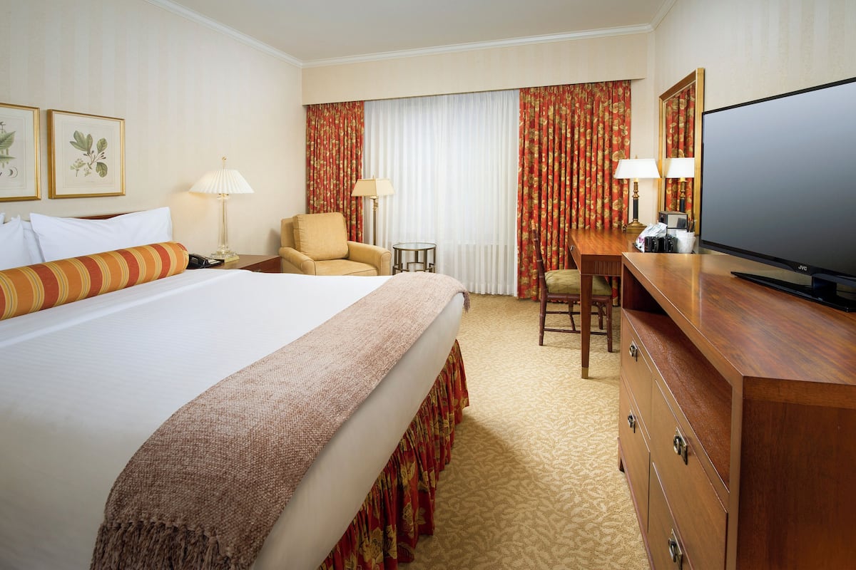 A hotel room with a large bed, a desk with a television, two chairs, and a small table.