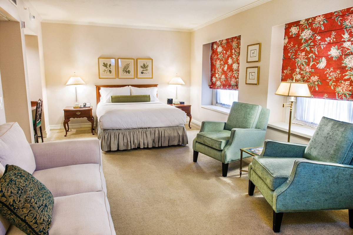A hotel room with a bed, two chairs, a sofa, and a window with floral curtains.