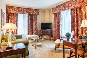 Una habitación de hotel con un sofá verde, un escritorio de madera, un televisor y cortinas con motivos florales.