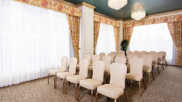 A conference room with rows of beige chairs, large windows with floral curtains, and a patterned carpet.