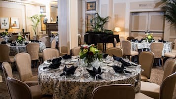 A formal dining room with round tables, each set with white tablecloths, black napkins, and floral centerpieces.