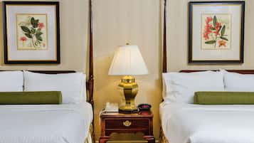 A hotel room with two beds, a nightstand with a lamp, a telephone, and framed botanical prints on the walls.