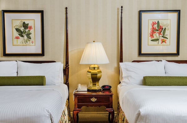 Habitación de hotel con dos camas, una mesita de noche con lámpara, teléfono e impresiones botánicas enmarcadas en las paredes.