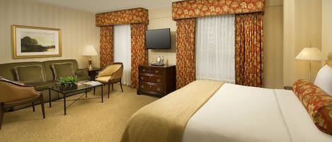 Une chambre d’hôtel avec un lit, un canapé, une chaise, une petite table avec une lampe, une télévision et des rideaux.