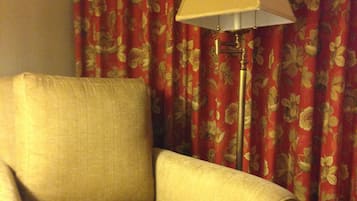 A beige armchair in a room with red floral curtains and a floor lamp.