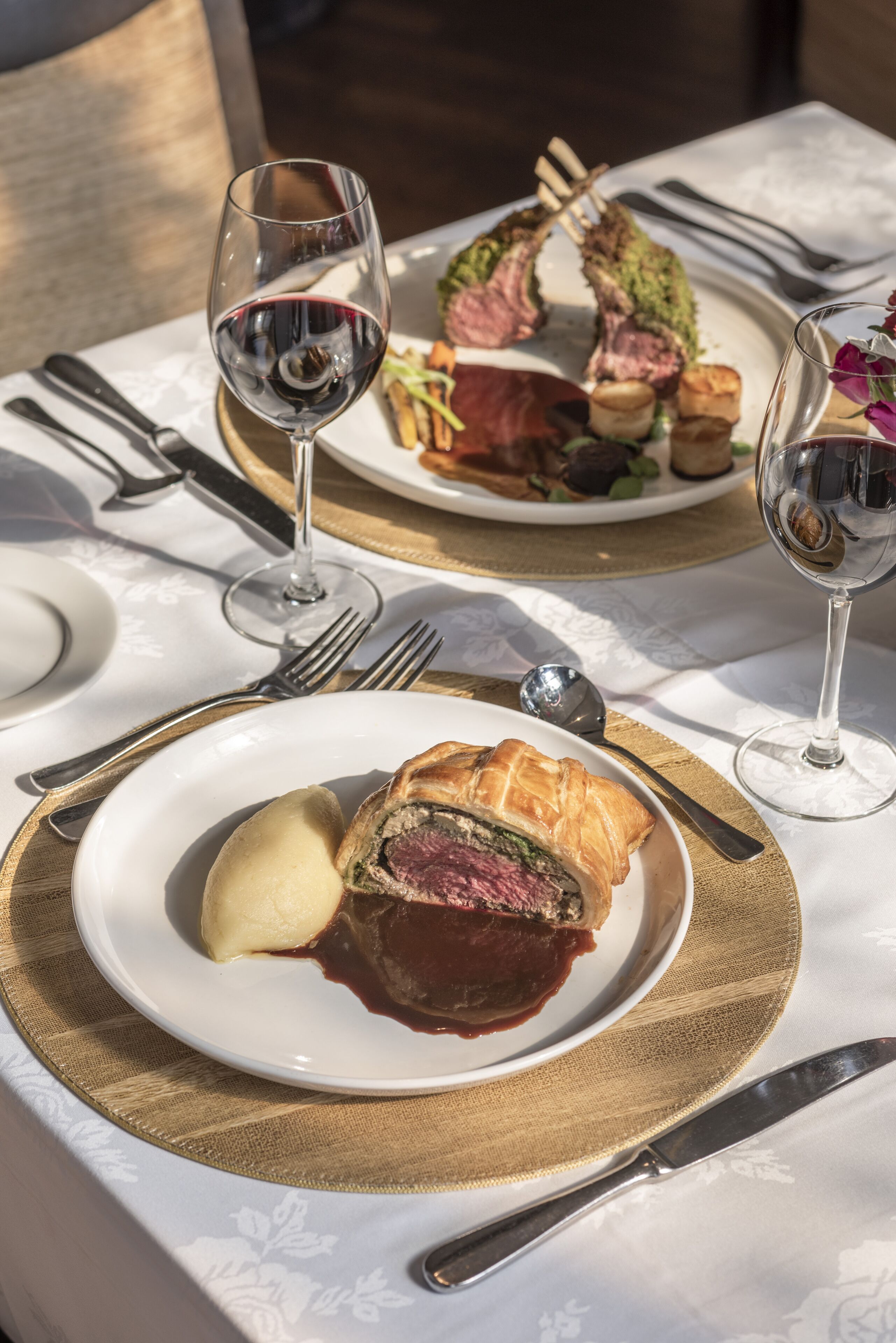 Uma mesa de jantar com pratos de comida, copos de vinho e talheres.