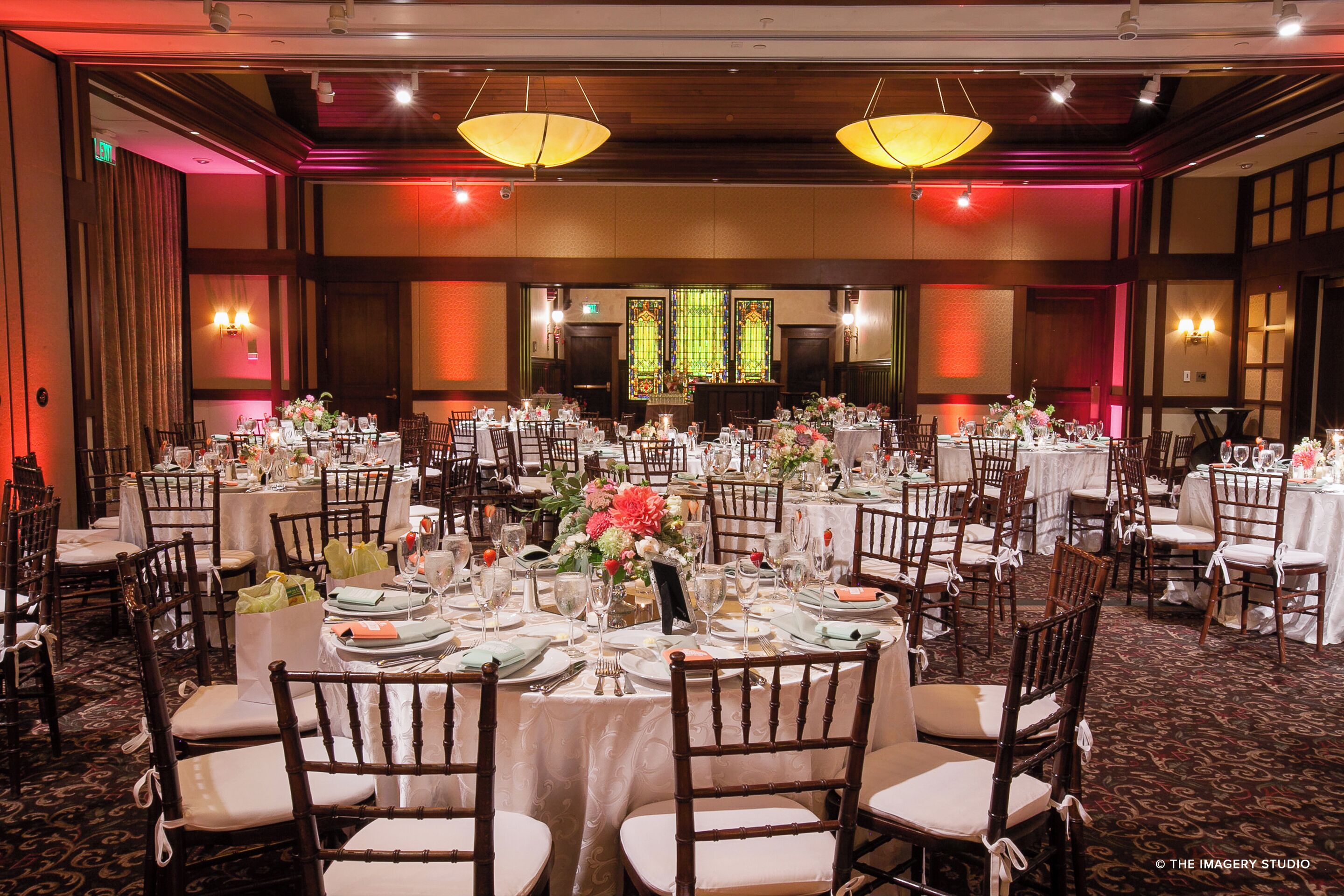 Un salón de banquetes con mesas redondas dispuestas para un evento formal, con centros de mesa florales y manteles blancos.