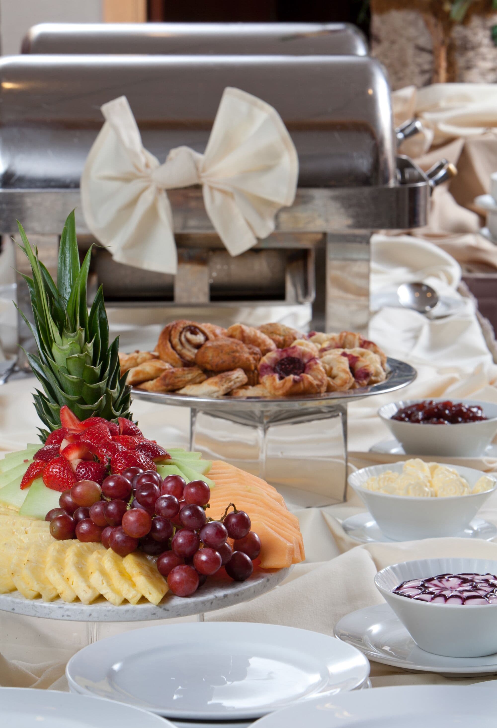 Una mesa de buffet con diversos alimentos, entre ellos frutas, pasteles y una parrilla.