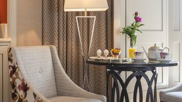 Una camera d'hotel con una poltrona decorata con motivi floreali, un tavolo con un vaso di fiori, una lampada e un servizio da tè.