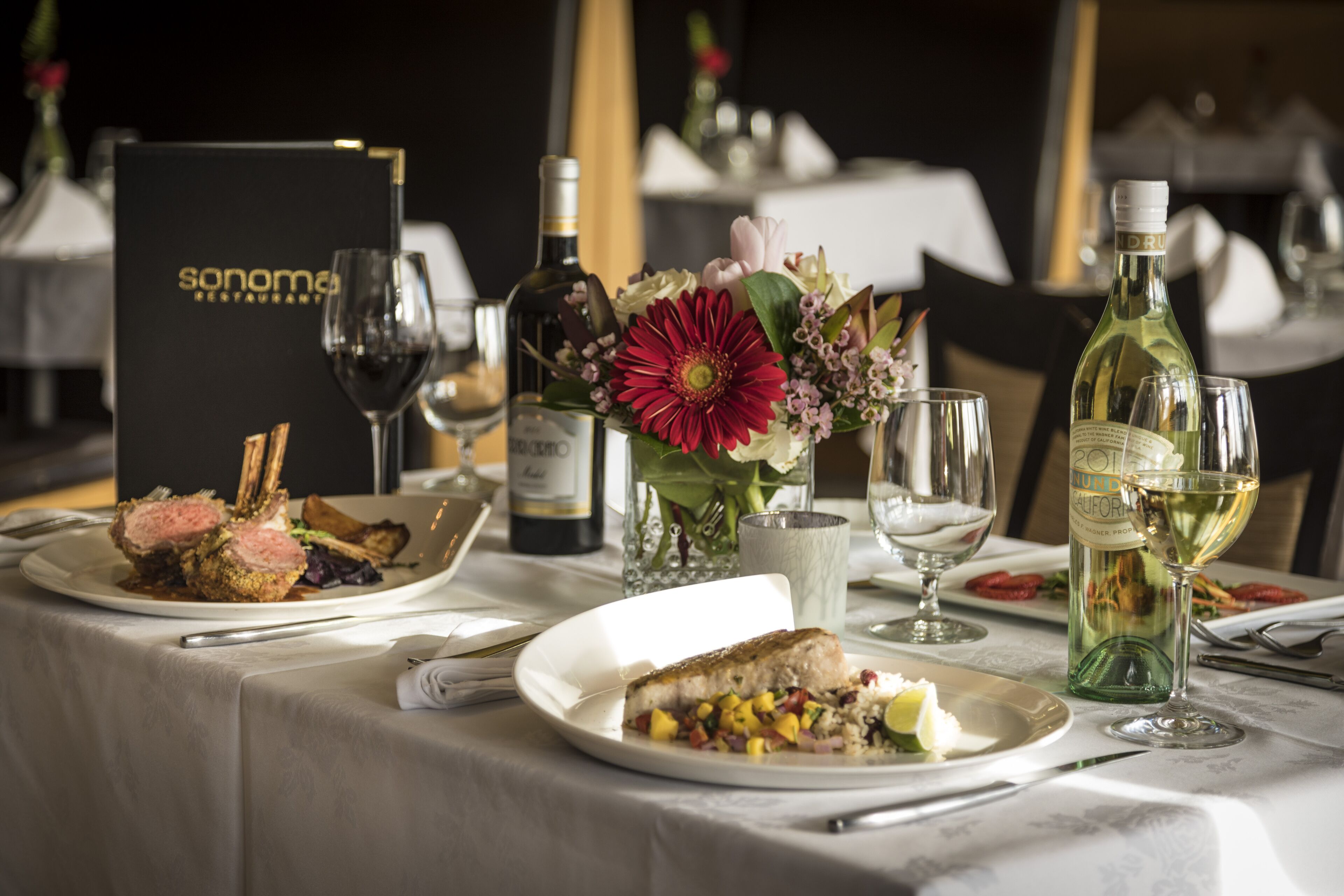 Una mesa de comedor dispuesta con platos de comida, copas de vino y un menú.