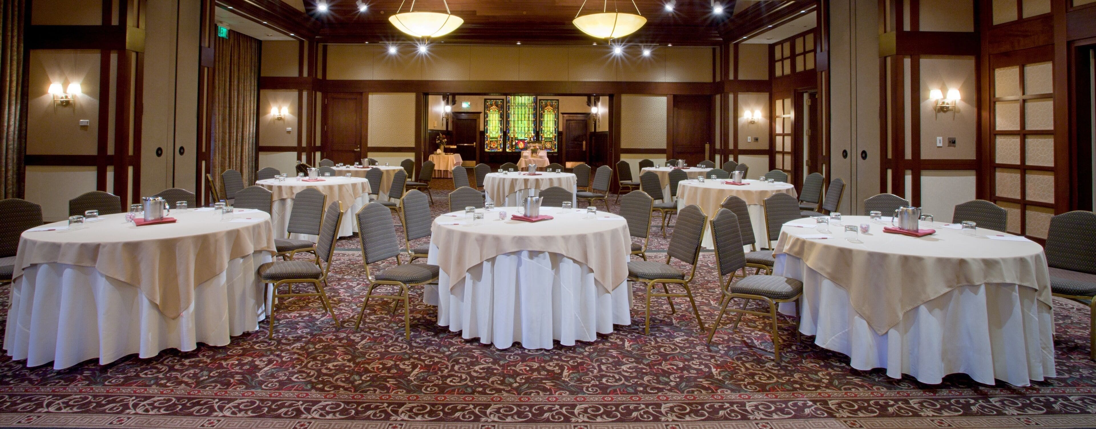 A conference room with round tables, chairs, and a carpeted floor.