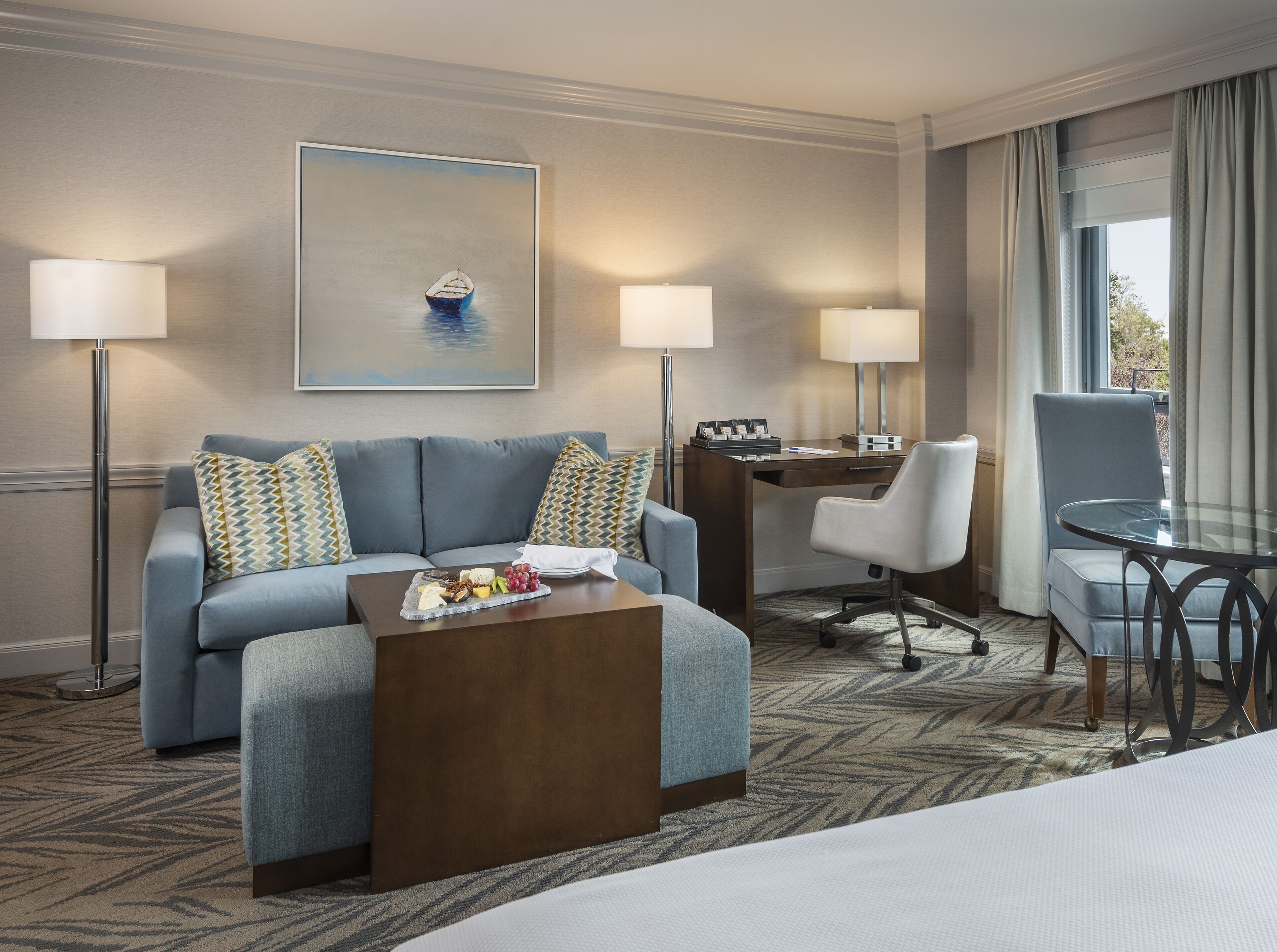 A hotel room with a sofa, a coffee table with snacks, a desk with a computer, and a chair.