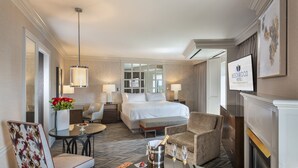 A hotel room with a bed, a sitting area with a table and chairs, a fireplace, and a television displaying the hotel name. - Beechwood Hotel (Worcester)