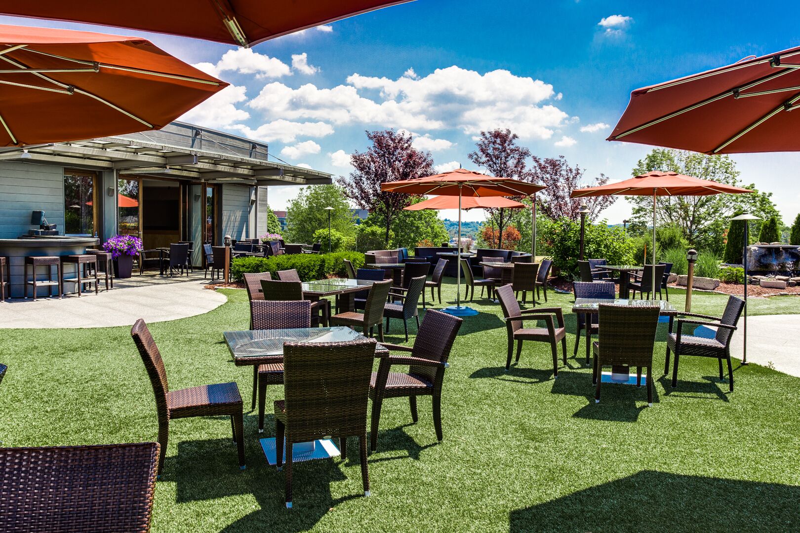 An outdoor patio area with multiple tables and chairs, umbrellas, and a bar area with a view of the surrounding landscape.
