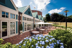 Een hotel met een patio met buiten zitplaatsen en een tuin met blauwe hortensia bloemen.