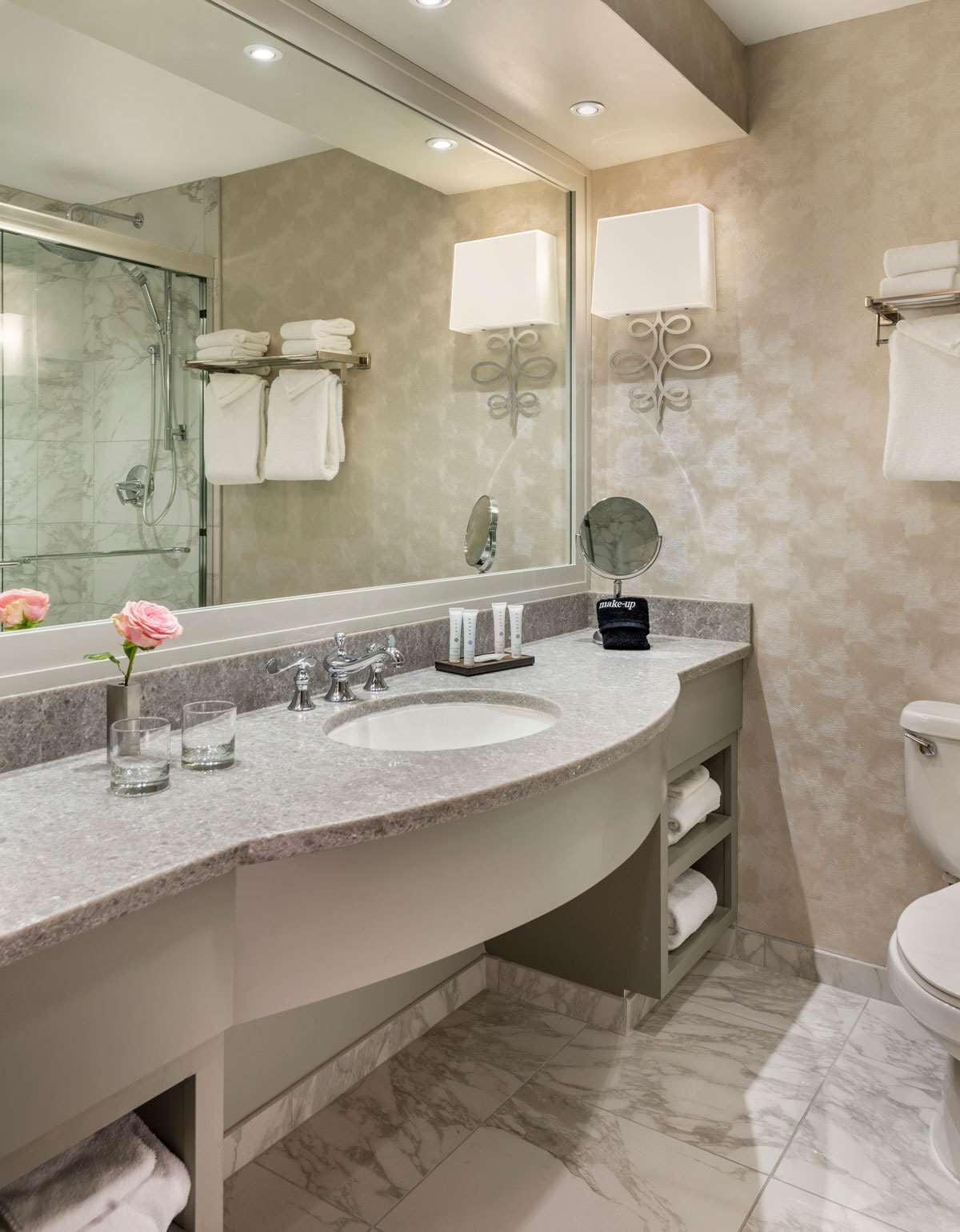 A modern bathroom with a curved vanity, a large mirror, a glass shower enclosure, and a toilet.