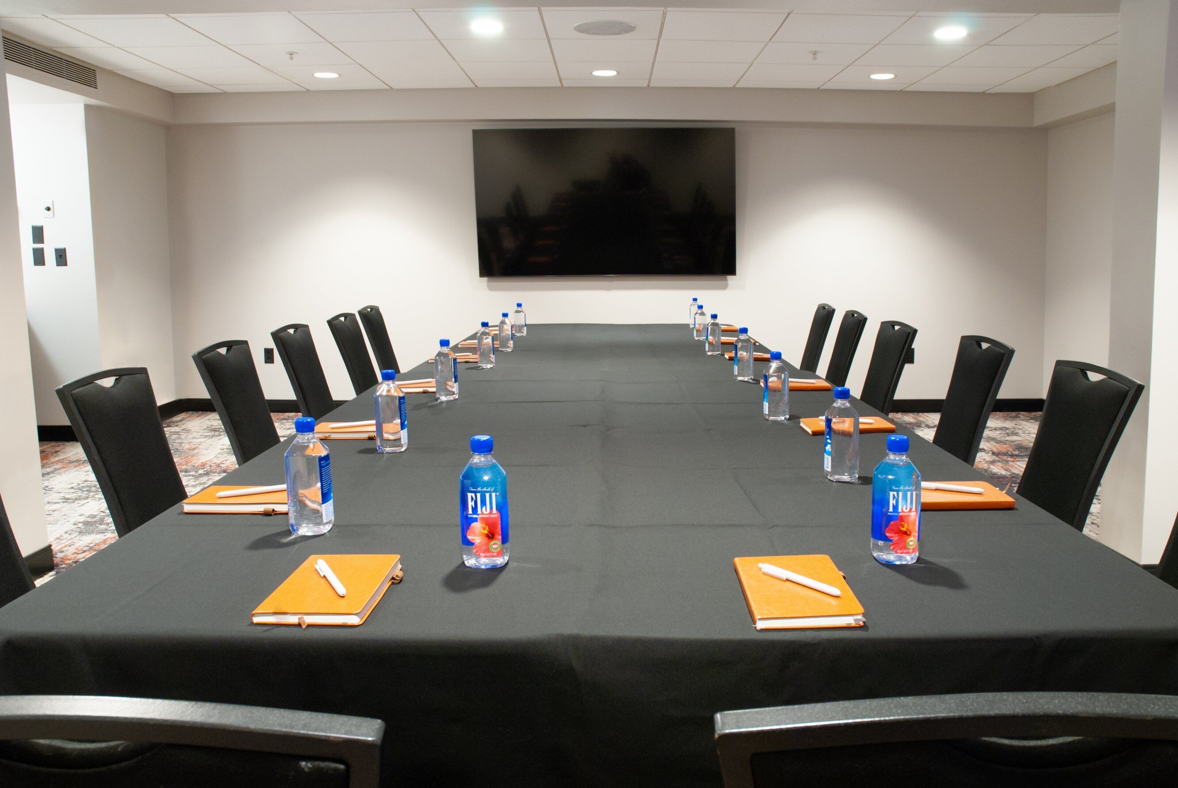 Une salle de conférence avec une longue table, des chaises, des bouteilles d’eau et des blocs-notes.