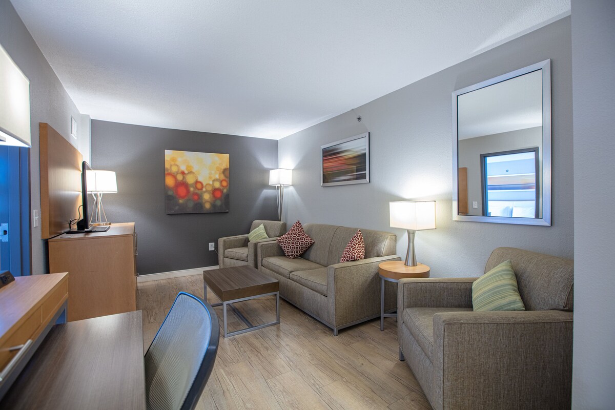 A modern living room with a sofa, armchairs, a coffee table, and a desk with a lamp.