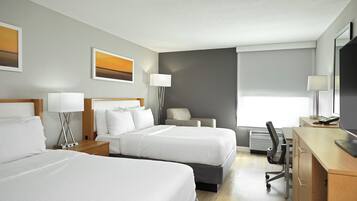 Ein Hotelzimmer mit zwei Betten, einem Schreibtisch, einem Sessel, einem Fernseher und einem Fenster mit Jalousien.
