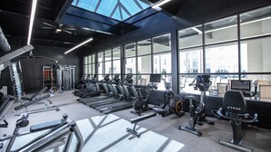 Ein Fitnessstudio mit verschiedenen Trainingsgeräten, großen Fenstern und einem Oberlicht.