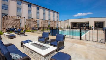 A rooftop patio with outdoor furniture, a pool, and a building with multiple windows.