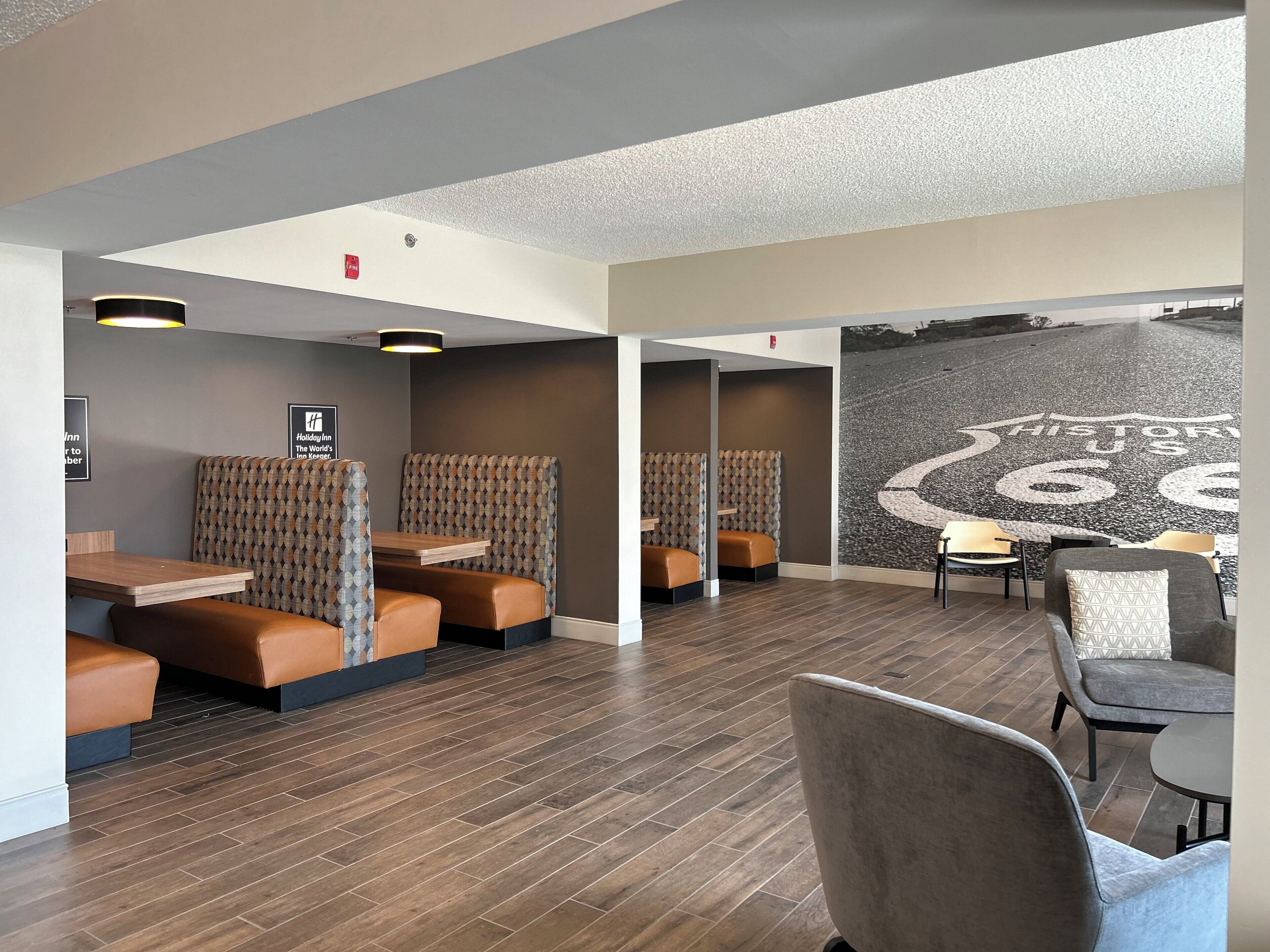 A modern hotel lobby with seating areas, wooden flooring, and a large mural on the wall.
