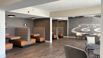 A modern hotel lobby with seating areas, wooden flooring, and a large mural on the wall.