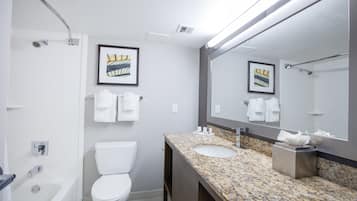 A modern bathroom with a white toilet, a sink with a granite countertop, and a shower. There are framed pictures on the wall and a towel rack with white towels.