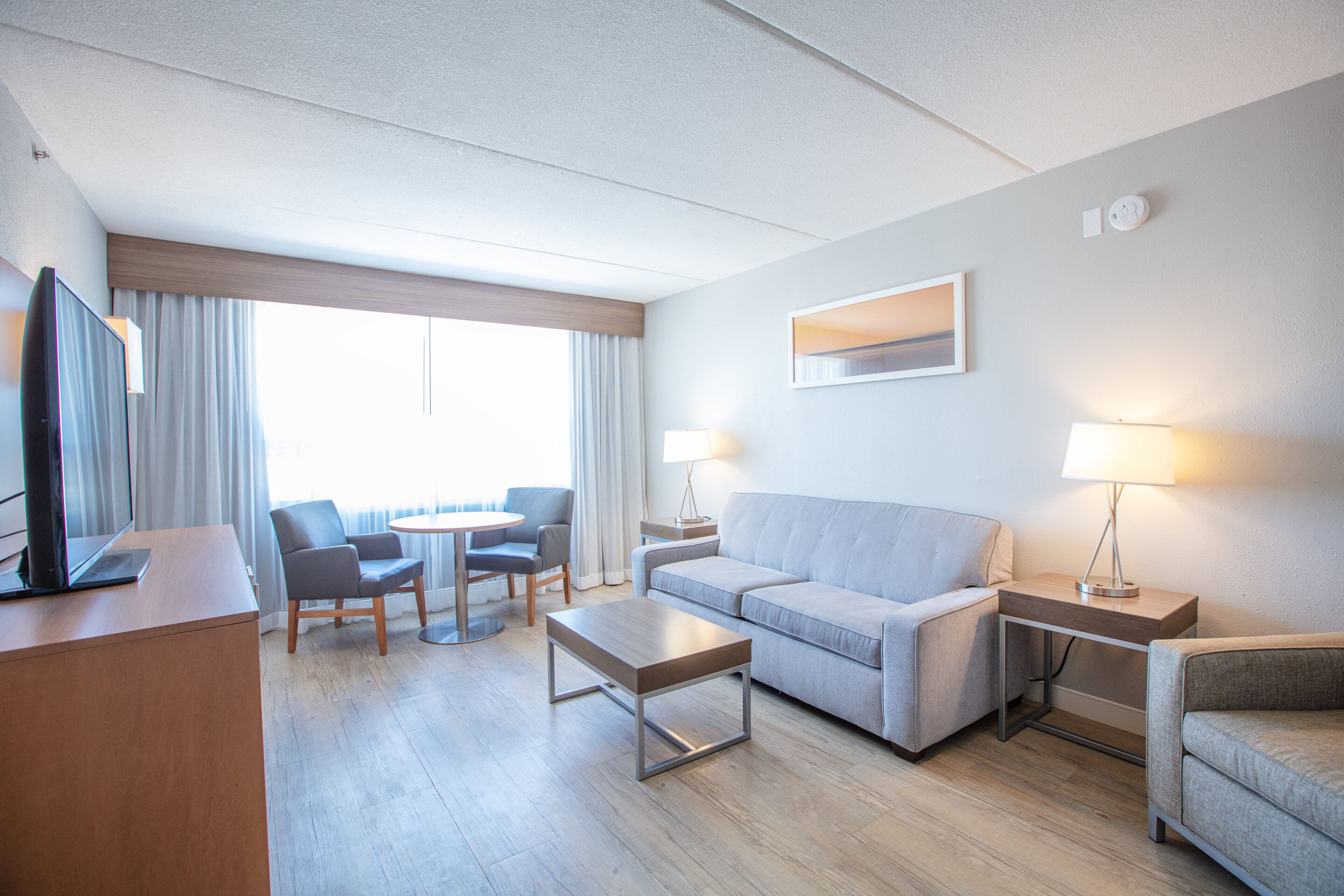 Ein modernes Hotelzimmer mit Flachbildfernseher, einer Sitzecke, einem Couchtisch und einem Schreibtisch mit Lampe.