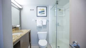Et moderne badeværelse med bordplade i granit, et hvidt toilet, et billede i ramme på væggen og en brusekabine i glas.