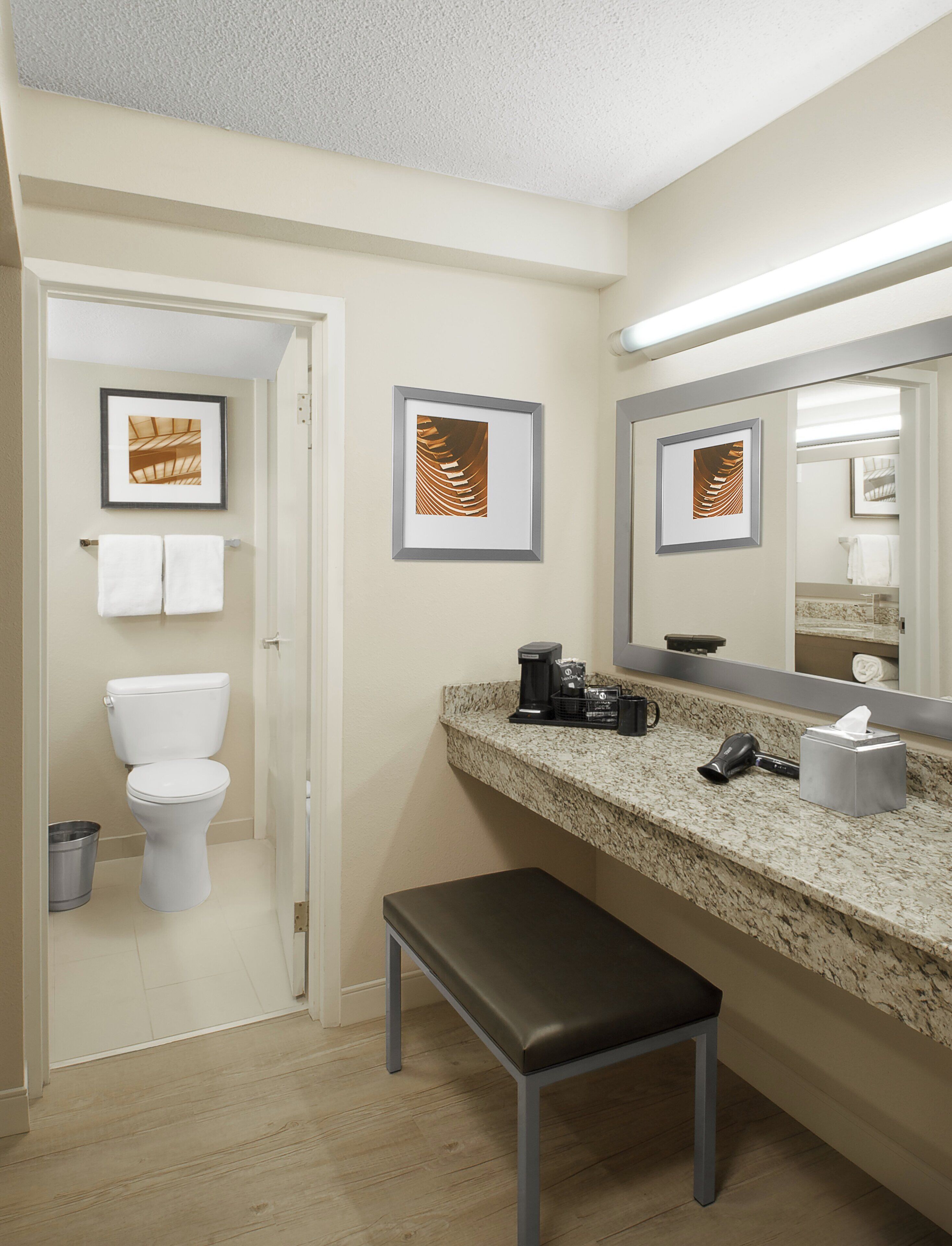 A bathroom with a toilet, a sink, a mirror, framed artwork, and a bench.