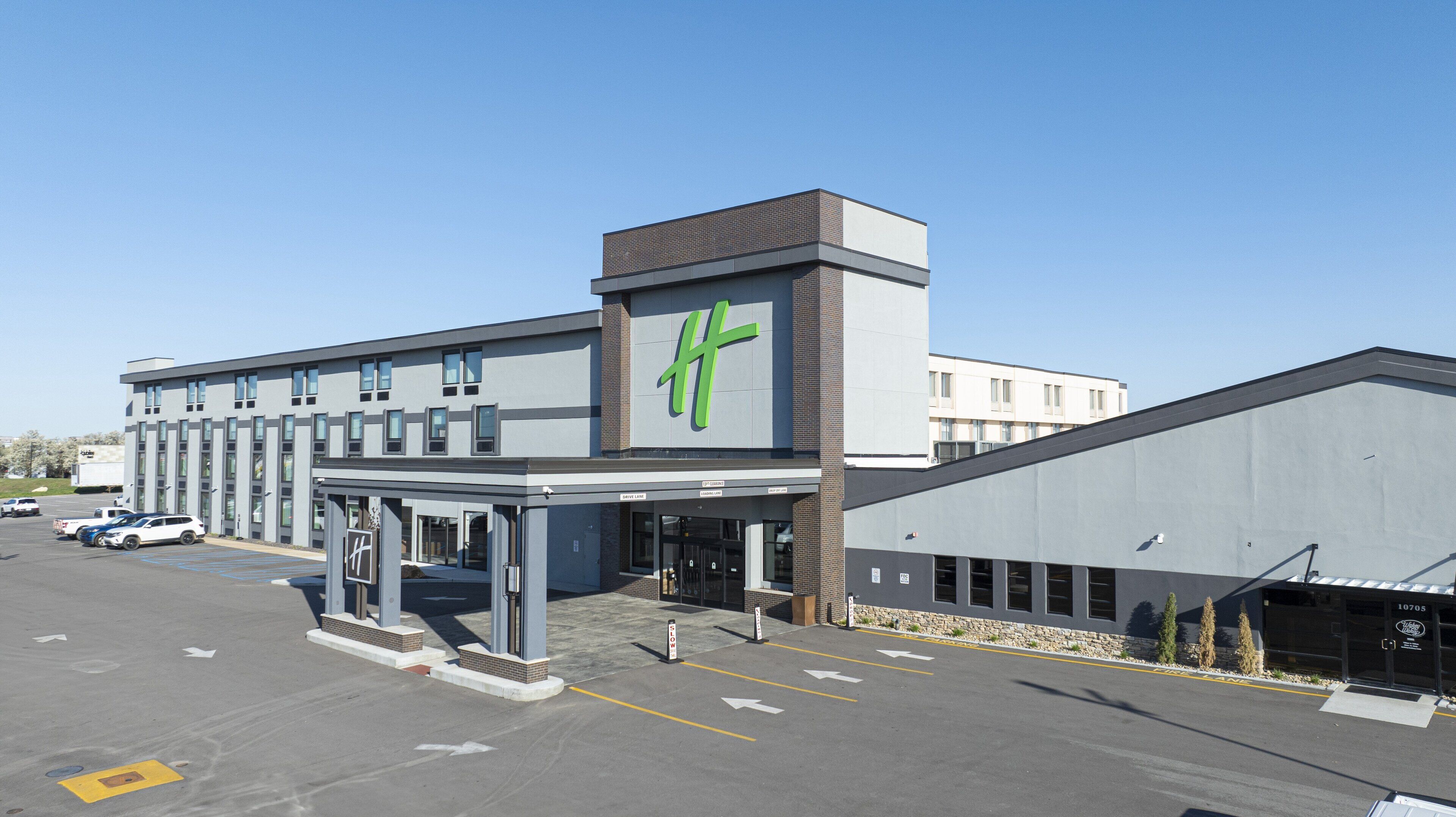 Hotel modern amb un logotip verd destacat, entrada coberta i aparcament.