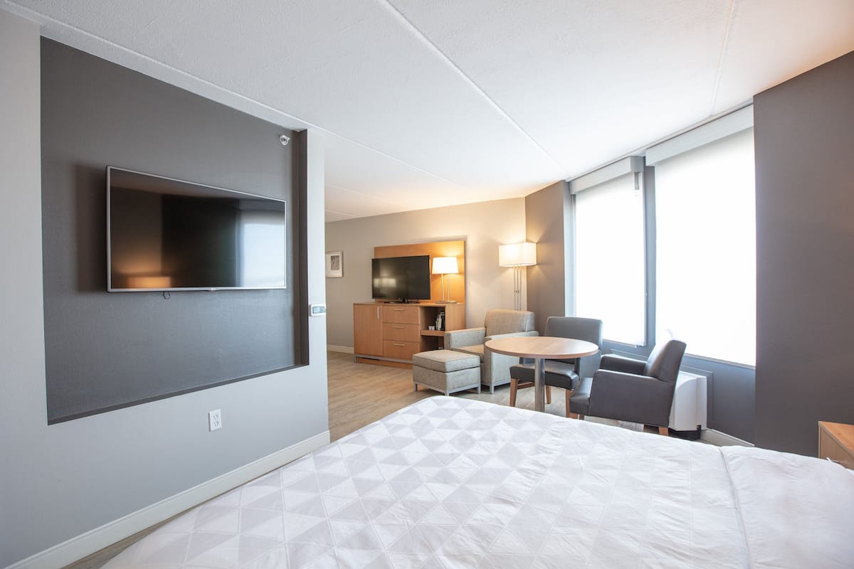 Habitació d'hotel moderna amb un llit gran, televisió de pantalla plana penjada a la paret, zona de dinar petita i zona de seients amb una làmpada.