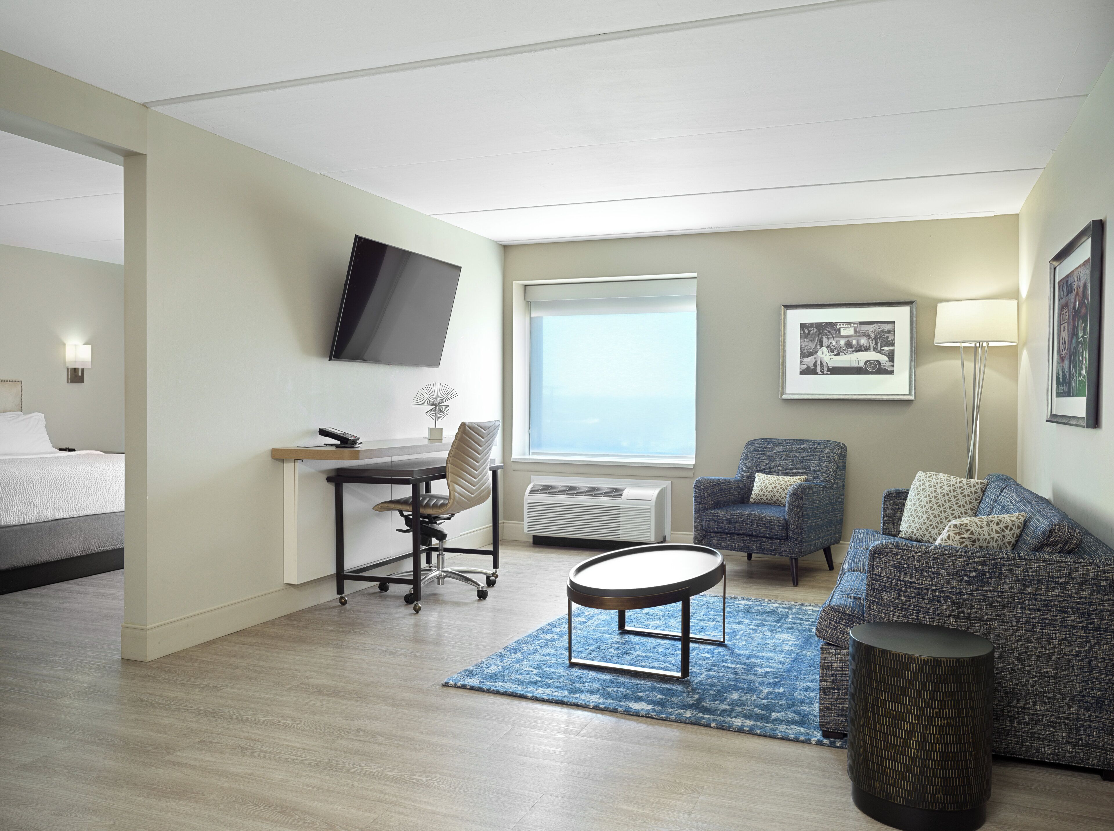 A hotel room with a bed, a desk with a chair, a sofa, a coffee table, a TV, and a window.