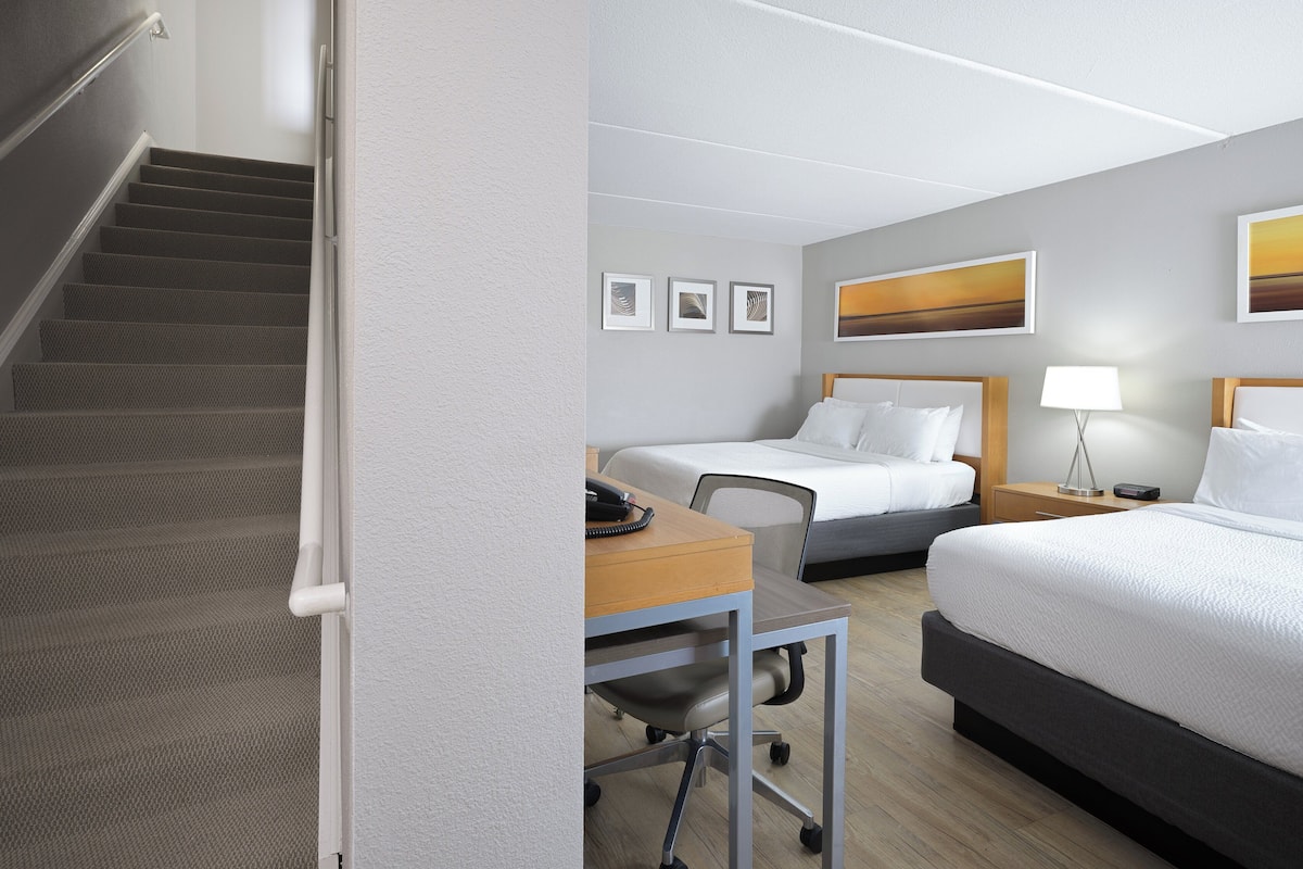 Habitació d'hotel amb llit, escriptori i cadira. Hi ha una escala que puja a la planta superior.