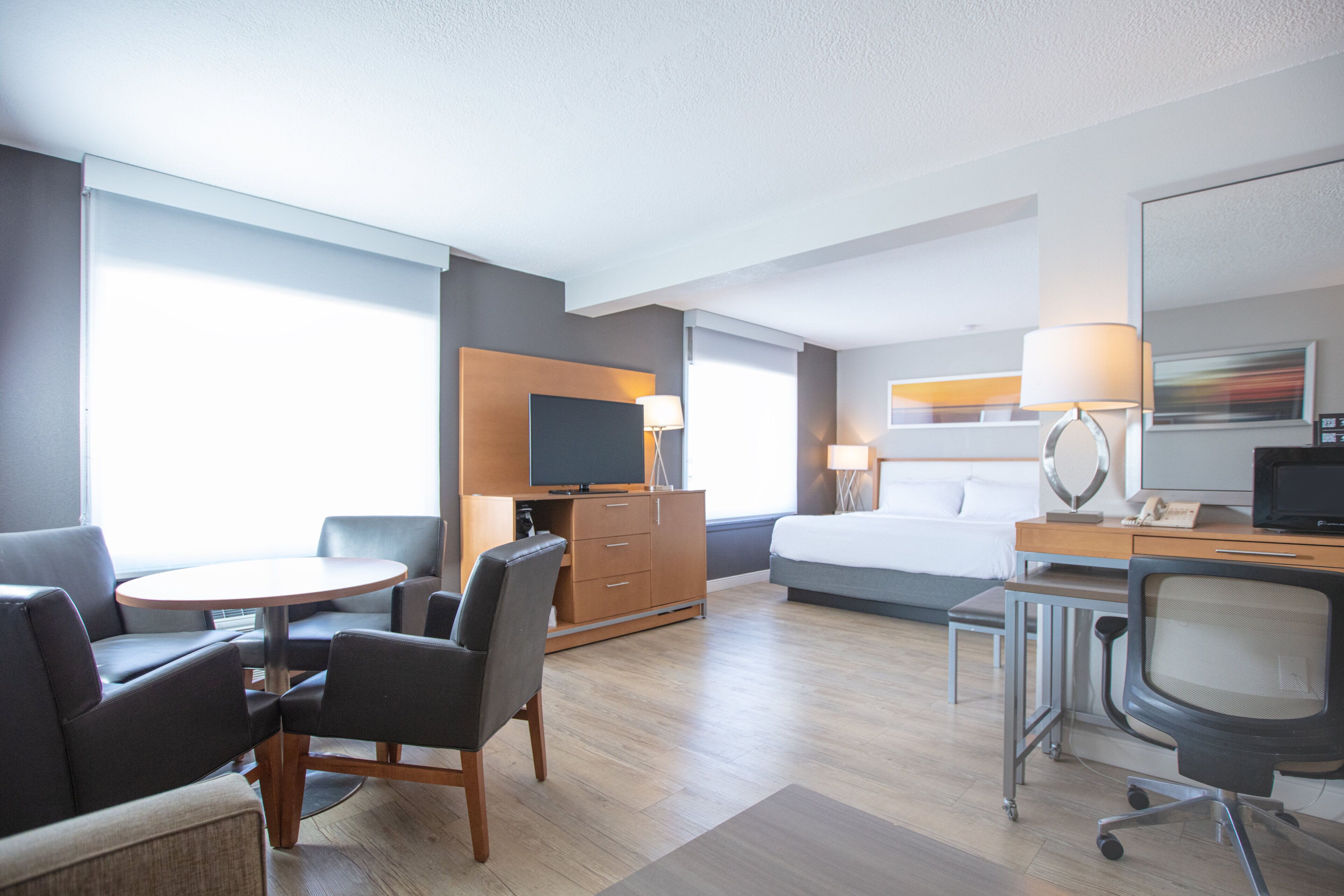 A hotel room with a bed, a desk, a chair, a television, and a sofa.