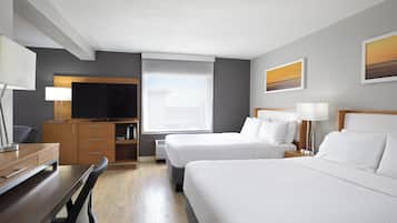 A hotel room with two beds, a desk, a TV, and a window.