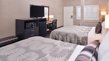 A hotel room with two beds, a desk with a television, a microwave, and a chair.